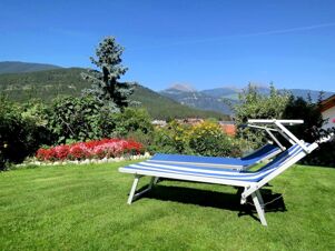 Blue and white striped lounge chair on green grass with colorful flowers and mountains in the background at Hotel Waldheim