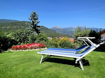 Blue and white striped lounge chair on green grass with colorful flowers and mountains in the background at Hotel Waldheim