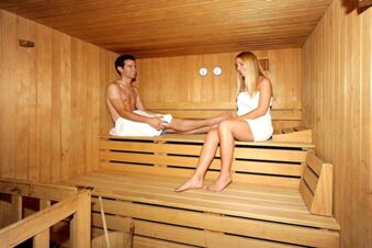 To personer slapper av i den trepanelkledde badstuen p&aring; Hotel Waldheim, omgitt av varmt treverk og badstueutstyr.