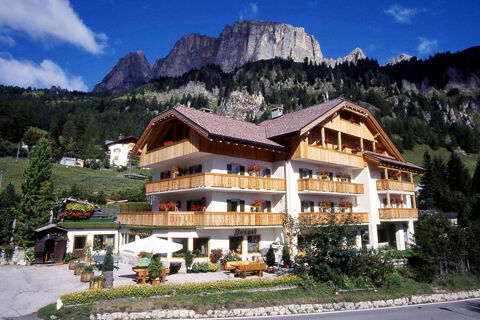 Hotel Gasthof Borest & Residence Riposo with balconies, flower boxes, outdoor seating, set against forested mountains and blue sky