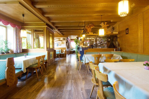 Wood-paneled dining room with wooden chairs, turquoise cushioned benches, white tablecloths, and decorative plants at Hotel Gasthof Borest & Residence Riposo