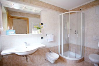 Bright bathroom with large wall mirror, sink, bidet, towel rack, and curved glass shower at Hotel Gasthof Borest & Residence Riposo