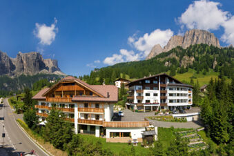 Two large alpine-style buildings with balconies and a garden near a road under blue sky at Hotel Gasthof Borest & Residence Riposo