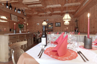 Dining area with wooden walls and ceiling, white tablecloth, red napkins, candles, wine bottles, and glasses at Hotel Gasthof Borest & Residence Riposo