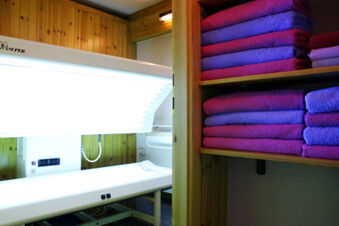 Stacked purple and pink towels on wooden shelves next to a tanning bed in a wooden-paneled room at Hotel Gasthof Borest & Residence Riposo