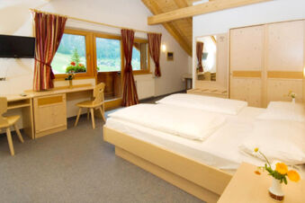 Bedroom with wooden furniture including bed, desk, chairs, wardrobe, TV, and windows with curtains in Hotel Gasthof Borest & Residence Riposo