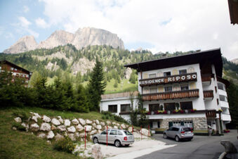Hotel Gasthof Borest & Residence Riposo building with parked cars, trees, rock wall, and mountainous background under cloudy sky
