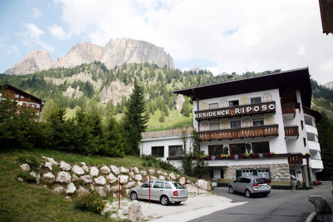 Hotel Gasthof Borest & Residence Riposo building with parked cars, trees, rock wall, and mountainous background under cloudy sky