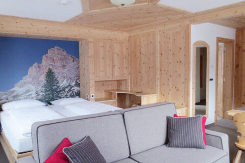 Hotel Gasthof Borest & Residence Riposo room with a wooden interior, gray sofa with pillows, bed, and mountain mural on wall