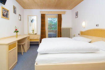 Hotel Gasthof Borest & Residence Riposo room with double bed, wooden furniture, desk, mirror, flowers, and window with curtains