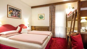 Hotel Maria room with twin beds and pink bedding, bunk bed, red carpet, two framed pictures, and a curtained window