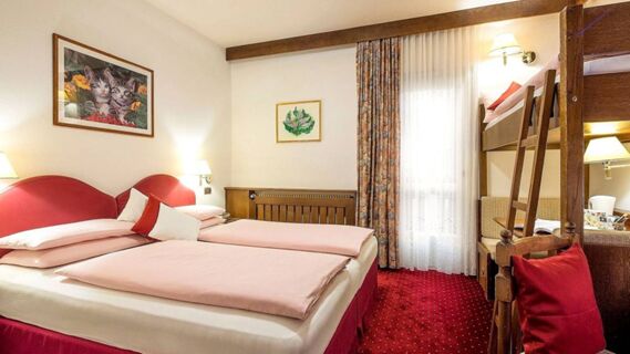 Hotel Maria room with twin beds and pink bedding, bunk bed, red carpet, two framed pictures, and a curtained window