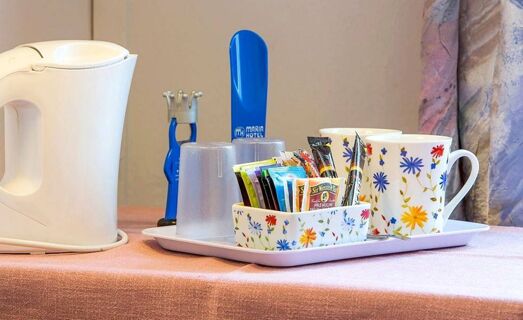 Gros plan sur un service &agrave; th&eacute; et &agrave; caf&eacute; &agrave; l'h&ocirc;tel Maria, avec une bouilloire, des tasses &agrave; motifs floraux et diff&eacute;rents sachets de th&eacute; sur un plateau.