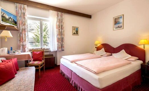 Chambre double lumineuse &agrave; l'h&ocirc;tel Maria avec deux lits simples, des accents rouges et une fen&ecirc;tre avec vue sur la montagne dans une atmosph&egrave;re confortable.