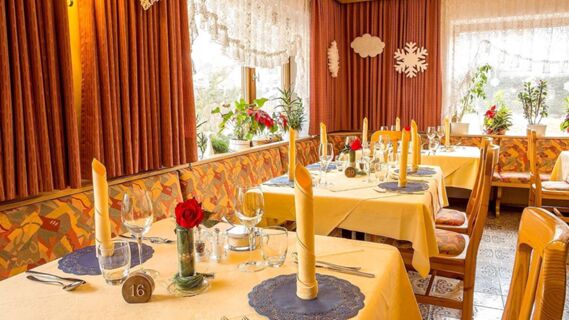 Dining area in Hotel Maria with tables set with yellow napkins, glassware, red flowers, and patterned bench seating
