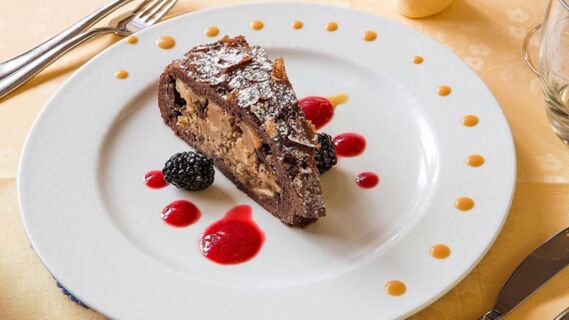 Une part de g&acirc;teau au chocolat avec des baies et une sauce rouge et orange servie sur une assiette blanche &agrave; l'h&ocirc;tel Maria.