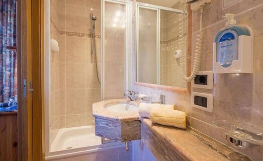 Bathroom in Hotel Maria with a shower area, mounted hairdryer, soap dispenser, sink, rolled towels, and a large mirror above the sink