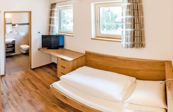 Bedroom at Residence Flamingo with single wooden bed, white bedding, TV on wooden desk, two windows, and entrance to bathroom