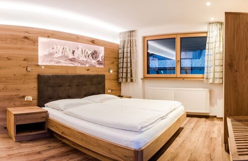 Bedroom at Residence Flamingo with wooden furniture, double bed, nightstand, window with curtains, and mountain artwork on wall