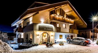 Residence Flamingo valgustatud hoonel on talvisel &ouml;&ouml;l lumine fassaad koos puidust balustraadide ja pidulike kaunistustega.