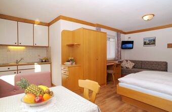 A studio room at Residence Flamingo with a bed, wooden wardrobe, kitchen area, table with fruit bowl, and a wall-mounted TV