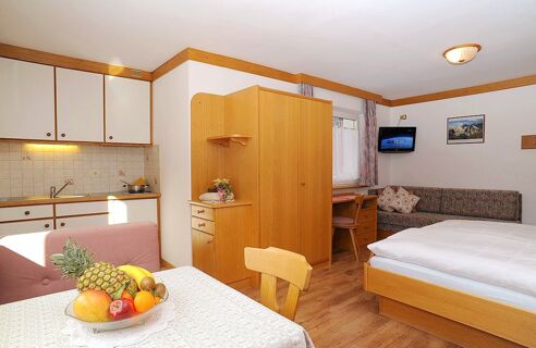 A studio room at Residence Flamingo with a bed, wooden wardrobe, kitchen area, table with fruit bowl, and a wall-mounted TV