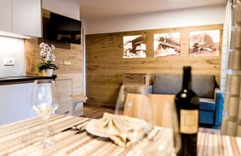 Dining table with wine bottle and glasses, sofa, wall-mounted TV, orchid plant, and wooden decor at Residence Flamingo