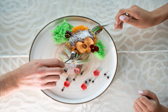 Two hands with spoons about to share a plated dessert with green sponge cake and dried apple at Hotel Fanes