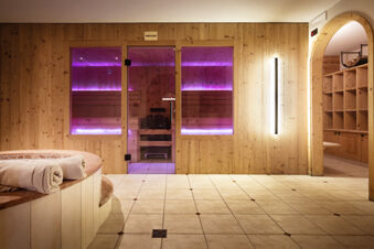 Wood-paneled Finnish sauna with purple LED lights inside and a tiled floor with towels on a round bench at Hotel Fanes