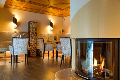 Cozy seating area with upholstered chairs and a lit fireplace next to a wood stack inside Hotel Fanes interior