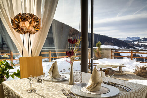 Table set with folded napkins, glassware, silverware, flower vase, and a decorative lamp at Hotel Fanes overlooking snow and mountains
