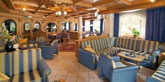 Mysig lounge med bl&aring;randiga soffor och tr&auml;m&ouml;bler i traditionell stil p&aring; Hotel Schwarzenbach med naturligt ljus.