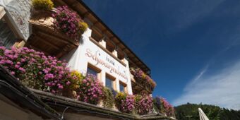 Den dekorativa fasaden p&aring; Hotel Schwarzenbach med sitt &ouml;verfl&ouml;d av f&auml;rgglada blommor under en klarbl&aring; himmel i alpin stil.