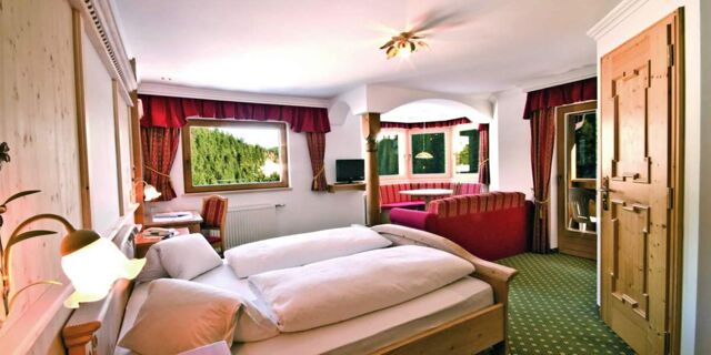 Hyggeligt hotelv&aelig;relse p&aring; Hotel Schwarzenbach med tr&aelig;m&oslash;bler, dobbeltseng, opholdsomr&aring;de og udsigt over et gr&oslash;nt skovlandskab.