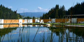 Naturlig simdamm med solstolar och gr&ouml;nt landskap i bakgrunden p&aring; Hotel Schwarzenbach f&ouml;r maximal avkoppling.