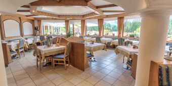Ljus och inbjudande restaurang i Hotel Schwarzenbach med tr&auml;m&ouml;bler, dukade bord och stora f&ouml;nster med utsikt &ouml;ver naturen.