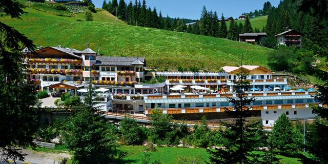 Hotel Schwarzenbach &auml;r pittoreskt bel&auml;get p&aring; en sluttning med m&aring;nga blommor p&aring; balkongerna och ett omgivande gr&ouml;nt landskap i bergen.