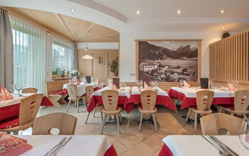 Dining area of Hotel Theiner with wooden chairs, tables covered in white and red cloths, and a large black and white wall photo