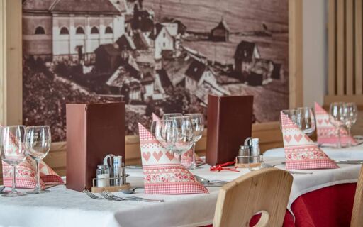 Table settings with folded patterned napkins, wine glasses, cutlery, and menus inside Hotel Theiner dining area