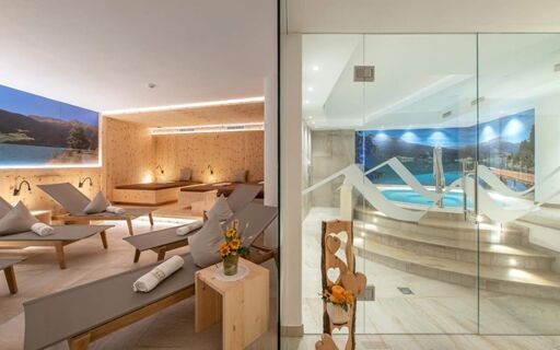 Moderne spa in Hotel Theiner met ontspannende ligstoelen, houten accenten en een whirlpool achter glas met bergmotieven.