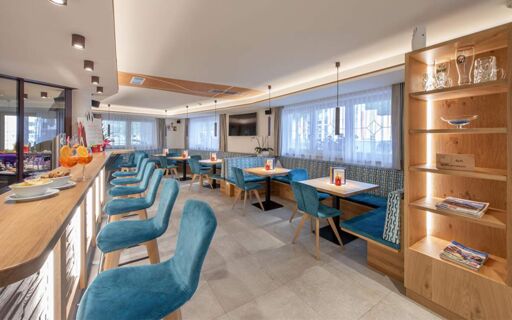 Modern hotel dining area at Hotel Theiner with blue upholstered chairs, wooden tables, and a wooden bar counter with stools