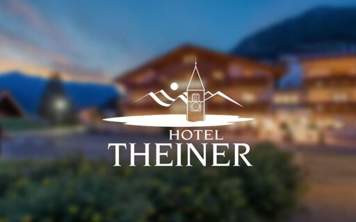 Het logo en de letters van Hotel Theiner zijn te zien tegen een vage achtergrond van een verlicht gebouw in de bergen bij schemering.