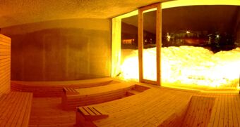 Wood-paneled sauna room with tiered wooden benches and large window showing snowy exterior at Hotel Alpenhof