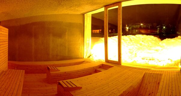 Wood-paneled sauna room with tiered wooden benches and large window showing snowy exterior at Hotel Alpenhof