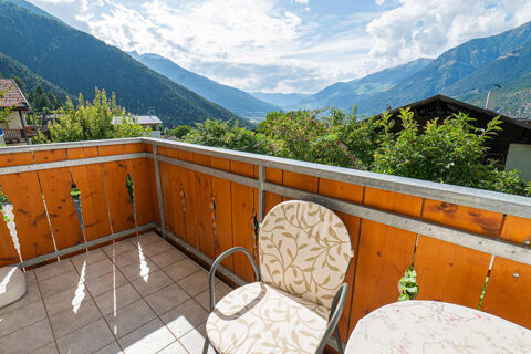Balcony at Residence Haus am Berg with tiled floor, a patterned cushioned chair, table, wooden railing, and mountain view