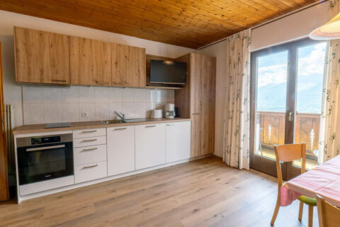 modern kitchen area with wooden cabinets, built-in oven, TV, and balcony doors at Residence Haus am Berg