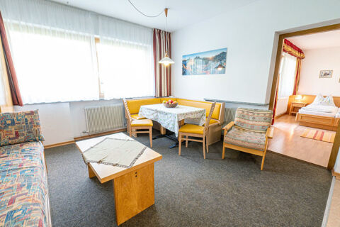 Living area with a yellow corner bench, dining table, chairs, patterned armchair, and couch in Residence Haus am Berg