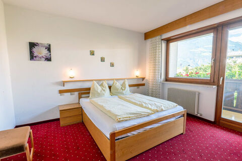 Bedroom interior of Residence Haus am Berg with double bed, wooden furniture, red carpet, and large window with mountain view