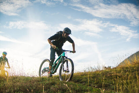 Two mountain bikers riding uphill on a grassy trail with cloudy sky in the background at Residence Haus am Berg