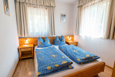 Double bed with blue starfish patterned bedding, two wooden nightstands, lamps, and large curtained windows in Residence Haus am Berg